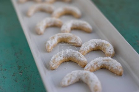 Foto de Vanillekipferl típico checo dulces galletas de Navidad para hornear, rollos de vainilla luna creciente con glaseado blanco en plato largo en filas - Imagen libre de derechos