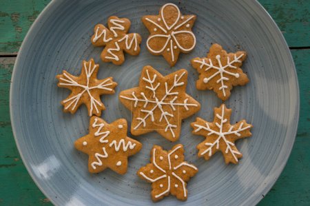 Photo for Painted traditional Christmas gingerbreads arranged on blue plate on old vintage painted table in daylight, various xmas shapes trees, stars and snowflakes - Royalty Free Image