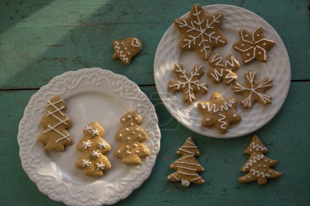 Photo for Painted traditional Christmas gingerbreads arranged on white plates on old vintage painted table in daylight, various xmas shapes trees, stars and snowflakes - Royalty Free Image