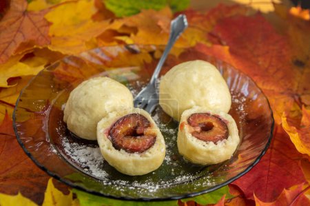 Photo for Plum dumplings cut in half on the plate on real autumnal colorful leaves with white sugar icing, tasty czech cuisine - Royalty Free Image