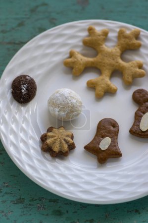 Various traditional Christmas sandbakelse, gingerbread, ball and vanillekipferl on white plates on old vintage painted table, various flavor shapes
