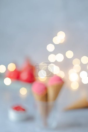 Foto de Helado rosa desenfocado en un cono de gofre sobre una mesa gris, guirnaldas de fondo bokeh. Postre congelado festivo. Foto de alta calidad - Imagen libre de derechos