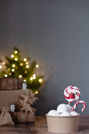 Foto de Helado vegano cremoso en una caja de papel con caramelos de Navidad sobre guirnaldas de fondo de luz. Decoraciones ecológicas. Cero residuos. Postre vegano festivo. Feliz Navidad. Foto de alta calidad - Imagen libre de derechos