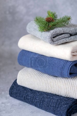 Foto de Una pila de ropa con suéteres decorados con una rama de árbol de Navidad con un cono sobre un fondo gris. Cambio de estación y guardarropa - Imagen libre de derechos