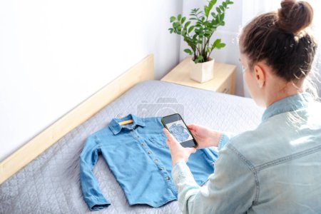 Eine Frau macht ein Foto mit dem Smartphone von ihrer eigenen Kleidung, um sie zu Hause online zu verkaufen. Altkleider. Ökologische und nachhaltige Mode. Hochwertiges Foto