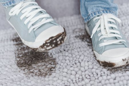 Téléchargez les photos : Fermez une paire de baskets sales avec une empreinte de pas sur le tapis gris propre à l'intérieur. Chaussures sales avec boue et terre. La vie quotidienne sale tache. Photo de haute qualité - en image libre de droit