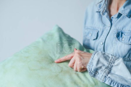 Weibliche Hand zeigt schmutzige Speichelflecken in Kissen für lange Verwendung. Reinigungskonzept. 