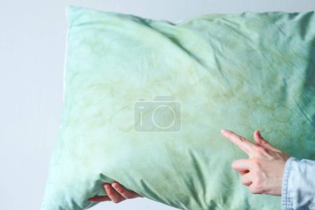 Mano femenina que señala manchas sucias de saliva en la almohada para un uso prolongado. Concepto de limpieza. Fuente de gérmenes o ácaros del polvo que llevan a enfermarse. Foto de alta calidad