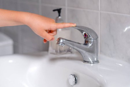 Téléchargez les photos : L'enfant ferme le robinet d'eau après des procédures hygiéniques. Le concept économise l'eau et protège l'environnement. Photo de haute qualité - en image libre de droit