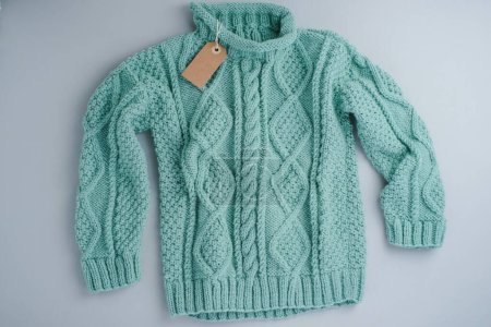 Pull turquoise Laine tricotée avec étiquette sur fond gris, isolée. Photo de haute qualité