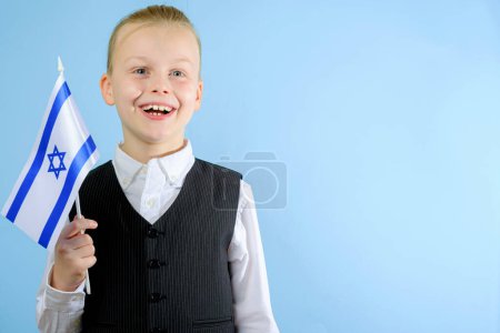 Foto de Niño lindo en un traje elegante sosteniendo la bandera de Israel sobre el fondo azul. Concepto patriótico. Concepto del Día de la Independencia. Foto de alta calidad - Imagen libre de derechos