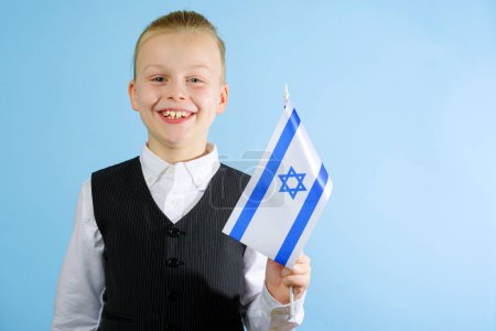 Foto de Niño lindo en un traje elegante sosteniendo la bandera de Israel sobre el fondo azul. Concepto patriótico. Concepto del Día de la Independencia. Foto de alta calidad - Imagen libre de derechos