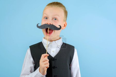 Foto de Niño divertido en un traje elegante con bigote en un palo con la boca abierta sobre el fondo azul. Concepto de celebración Purim. Fiesta de carnaval judío. Foto de alta calidad - Imagen libre de derechos