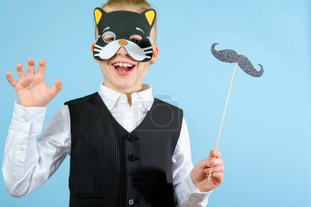 Foto de Un niño elegante con traje y máscara de gato de carnaval y con bigote en un palo sobre el fondo azul. Concepto de celebración Purim. Fiesta de carnaval judío. Foto de alta calidad - Imagen libre de derechos