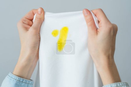 Unrecognizable woman holding white clothes with a yellow stain. Spoiled clothes food or a pet. daily life stain concept. top view. High quality photo