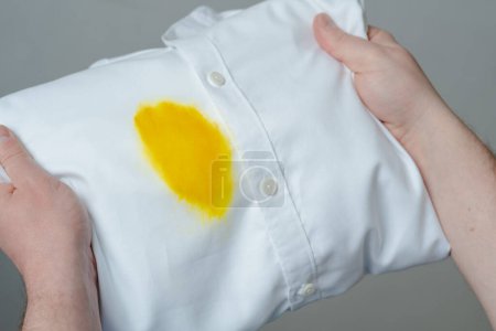 Manos de persona mostrando y evaluación visual mancha de grasa amarilla sucia en camisa blanca de accidente inesperado. Ropa estropeada. concepto de manchas de la vida diaria. Vista superior. Foto de alta calidad