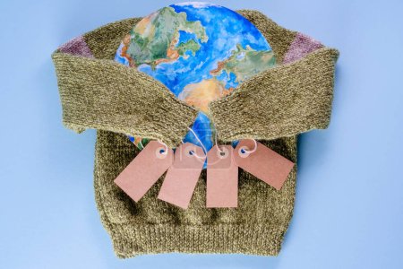 Creative concept buy less and overconsumption. The sweater sleeves holding the tags in the embrace of the planet on a blue background. Responsible consumption. top view. High quality photo