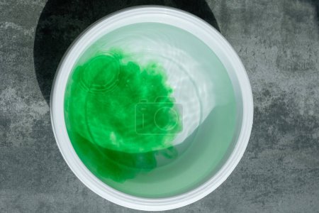 Ein weißes Becken mit grün gefärbtem Wasser auf Betongrund. Falscher Eindruck einer Firma oder eines Produkts. Greenwashing-Konzept. Ansicht von oben. Hochwertiges Foto