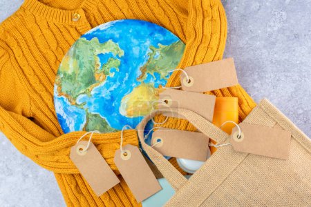 The sweater sleeves yellow holding in the embrace of the planet with an eco bag and tags. Responsible consumption. Creative concept buy less and overconsumption. top view. High quality photo