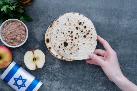 Human hands holding handmade round Matzah in a plate on a concrete background. Saved Jewish Pesach Tradition. Jewish Passover celebrations. top view. High quality photo