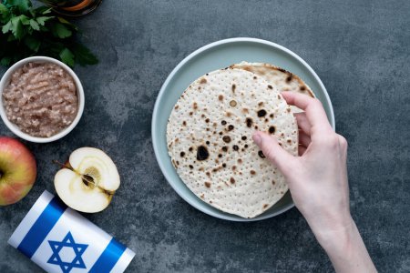 Human hands holding handmade round Matzah in a plate on a concrete background. Saved Jewish Pesach Tradition. Jewish Passover celebrations. top view. High quality photo
