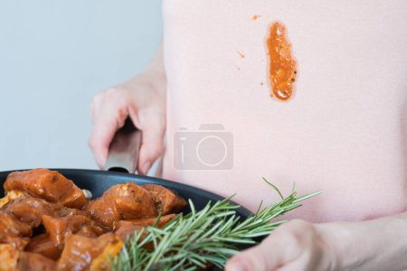 Ein schmutziger Fleck Soße oder Tomate auf rosa Kleidung. Unerkennbare Frau mit mariniertem Fleisch zum Grillen mit Kräutern und Gewürzen. Alltagskultur. Hochwertiges Foto