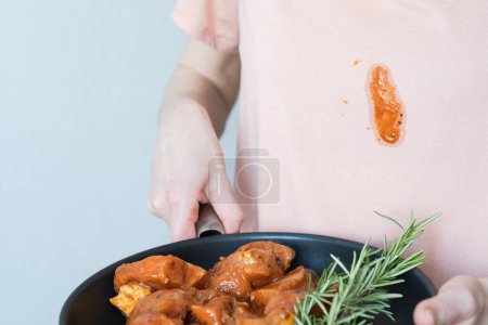Ein schmutziger Fleck Tomatensauce auf rosa Kleidung. Unerkennbare Frau mit mariniertem Fleisch zum Grillen mit Kräutern und Gewürzen. Alltagskultur. Hochwertiges Foto