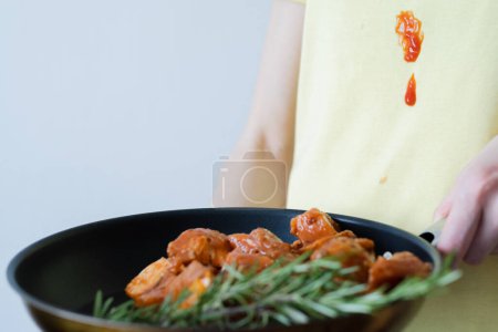 Tomatensauce auf gelbe Kleidung schütten. Unerkennbare Frau mit mariniertem Fleisch zum Grillen mit Kräutern und Gewürzen. Alltagskultur. Hochwertiges Foto