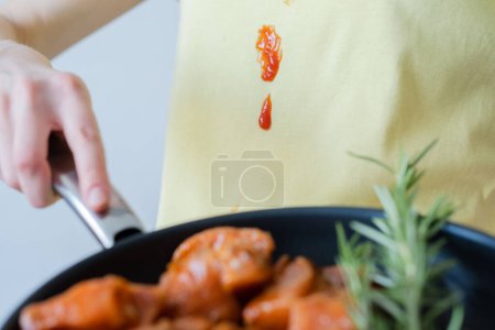 Spill tomato sauce or ketchup on yellow clothes. An unrecognizable person a frying pan with meat and herbs. daily life stain concept. High quality photo