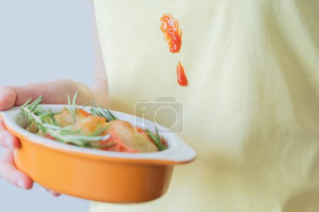 Verschüttete Tomatensauce oder Ketchup auf gelber Kleidung aus nächster Nähe. Eine bis zur Unkenntlichkeit verkleidete Frau hält einen Teig in ihren Händen. Alltagskultur. Hochwertiges Foto