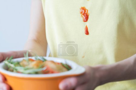 Aus nächster Nähe fallen Tomatensauce oder Ketchup auf gelbe Kleidung. Eine unkenntliche Person hält Salat in der Hand. Alltagskultur. Hochwertiges Foto