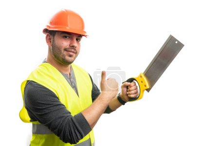 Photo for Builder man with cheerful smiling friendly expression holding lumber saw making thumb-up like gesture isolated on white studio background - Royalty Free Image