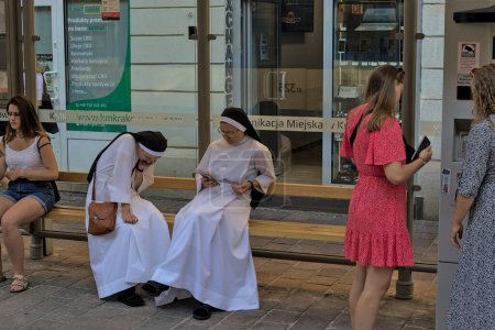 Téléchargez les photos : Krakow, Poland - July 24, 2022:Two nuns in white robes use smartphones. The nuns settled down at the city tram stop in the historic center of the city. - en image libre de droit