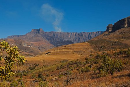 La fumée monte d'un feu de brasier au-dessus de la formation de l'amphithéâtre dans le parc national royal du Natal dans le Drakensberg Afrique du Sud