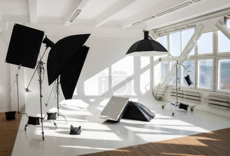 Professional lighting equipment, flashes, c-stands on a cyclorama in modern photo studio with a huge windows. Octabox, stripbox, softbox, buety plate and other stuff for photography