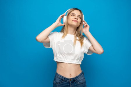 Foto de Joven mujer rubia con auriculares escuchando música .Music chica adolescente bailando sobre fondo azul aislado - Imagen libre de derechos