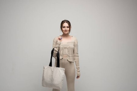 Photo for Brunette cheerful millennial woman holding white eco bag standing over white studio background. Concept of recycle for better environment. No plastic. Fashion and ecology concept - Royalty Free Image