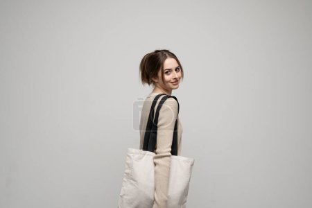 Photo for Happy, smiling brunette young woman carrying reusable cotton bag. Concept of recycle for better environment. No plastic - Royalty Free Image
