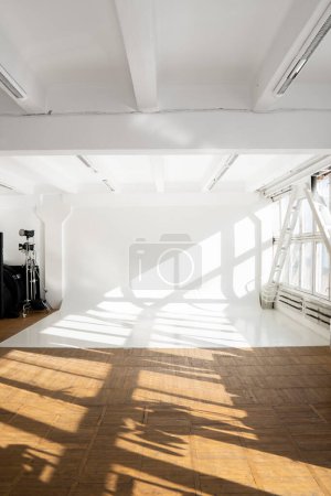 Téléchargez les photos : Nettoyez un grand cyclorama blanc dans un studio photo avec une lumière du soleil et des ombres depuis une grande fenêtre. Plain mur studio photo vide - en image libre de droit