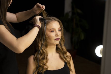 Professionelle Friseurin frisiert lange weibliche Haare mit Lockenstab und macht Styling für weibliche Kunden. Schönheitssalon