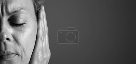 woman suffering from deafness and hearing loss on grey background