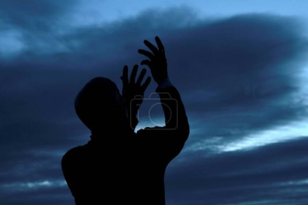 Photo for Black man praying to god with arms outstretched looking up to the sky - Royalty Free Image