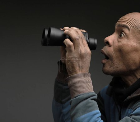 Photo for Man looking through binoculars with grey black background - Royalty Free Image