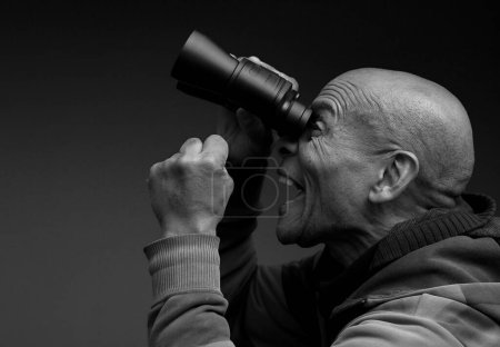 Téléchargez les photos : Homme regardant à travers des jumelles avec fond gris noir - en image libre de droit