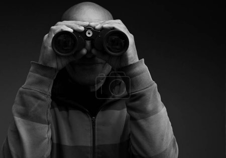 Foto de Hombre mirando a través de prismáticos con fondo negro gris - Imagen libre de derechos