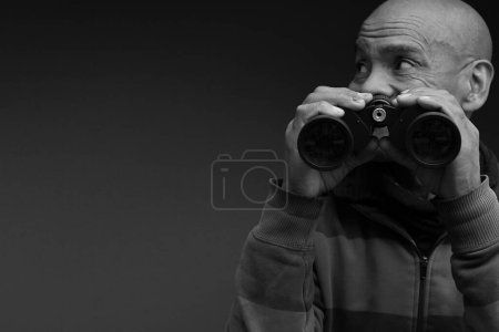 Foto de Hombre mirando a través de prismáticos con fondo negro gris - Imagen libre de derechos