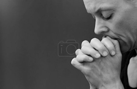 Foto de Mujer rezando con las manos dobladas sobre fondo gris negro - Imagen libre de derechos