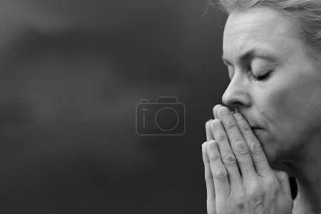 Foto de Mujer rezando con las manos dobladas sobre fondo gris negro - Imagen libre de derechos