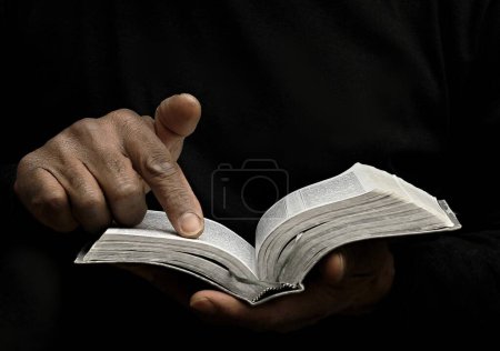 Photo for Black man praying god with bible in hands. Caribbean man praying on black background, cropped section - Royalty Free Image