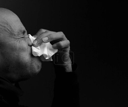 Man with flu. man blowing nose after catching a cold, black and white studio shot 